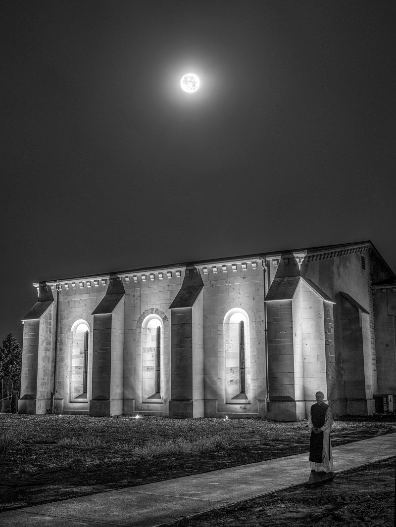 Full moon over Abbey Church, while monk strolls a moon-lit path