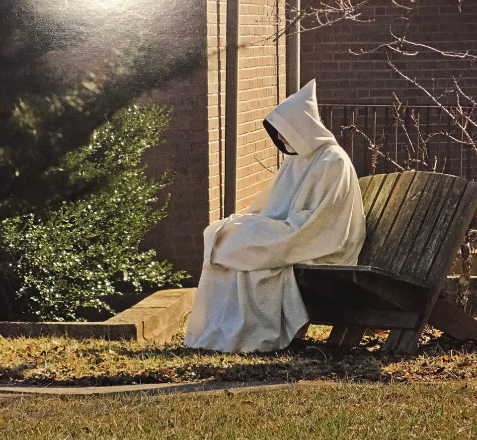 Trappist monk is white cowl sits in prayer
