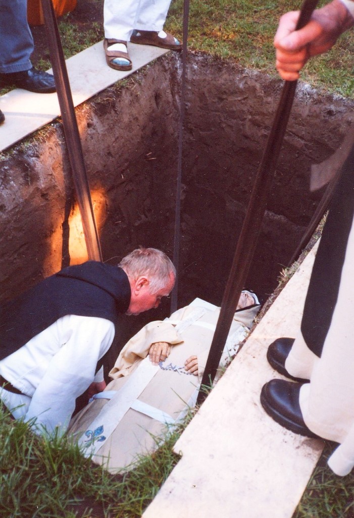 a deceased monk is lowered into a grave