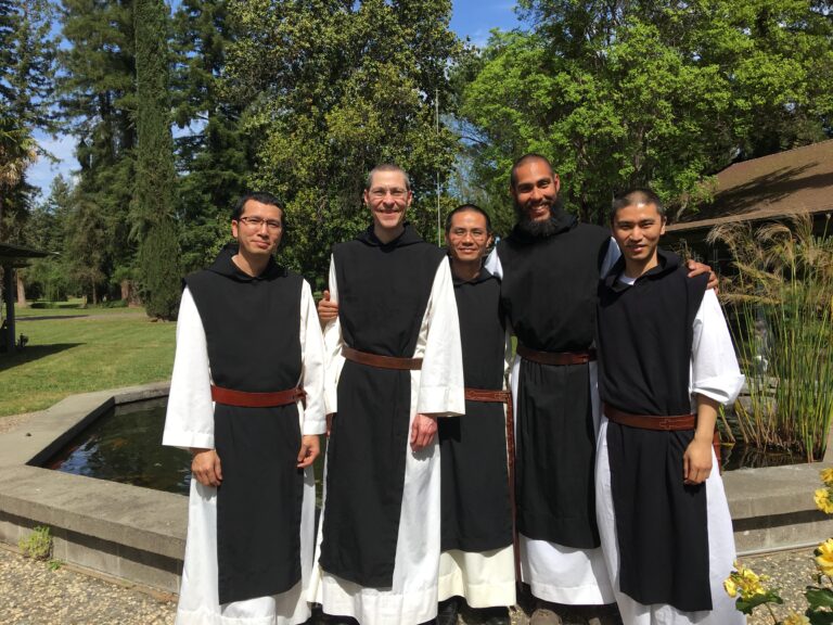 A group of smiling Trappist monks pose in front of a garden fountain